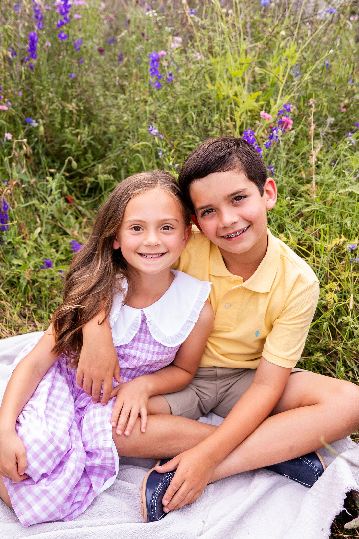 two siblings sitting on a blanket in a wild flower field in plano