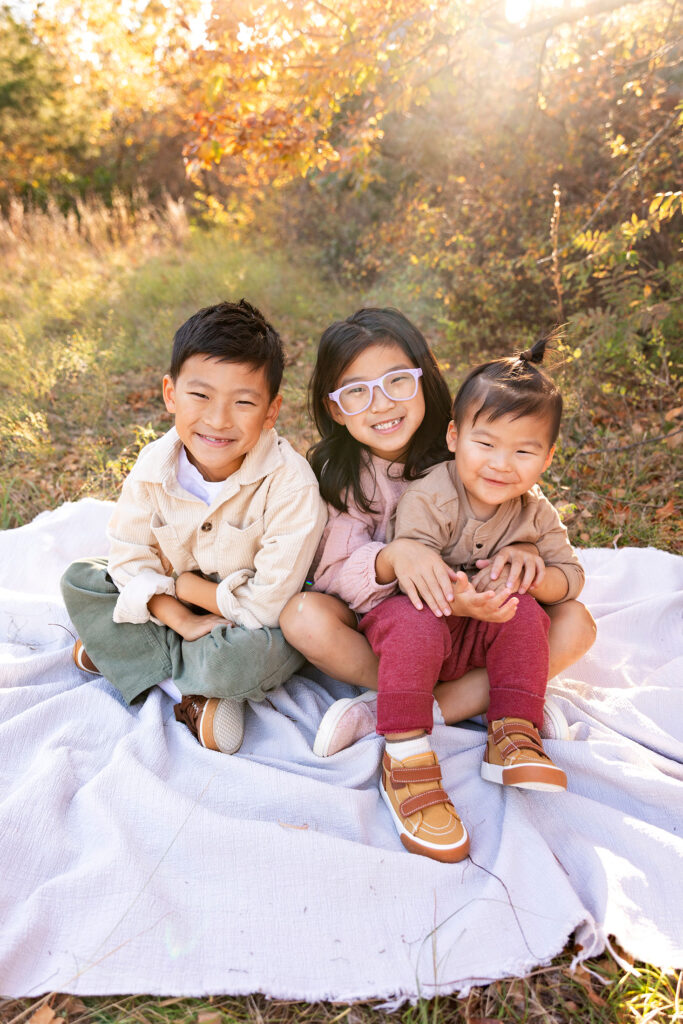 three cute kids sitting on a blanket during their fall mini session