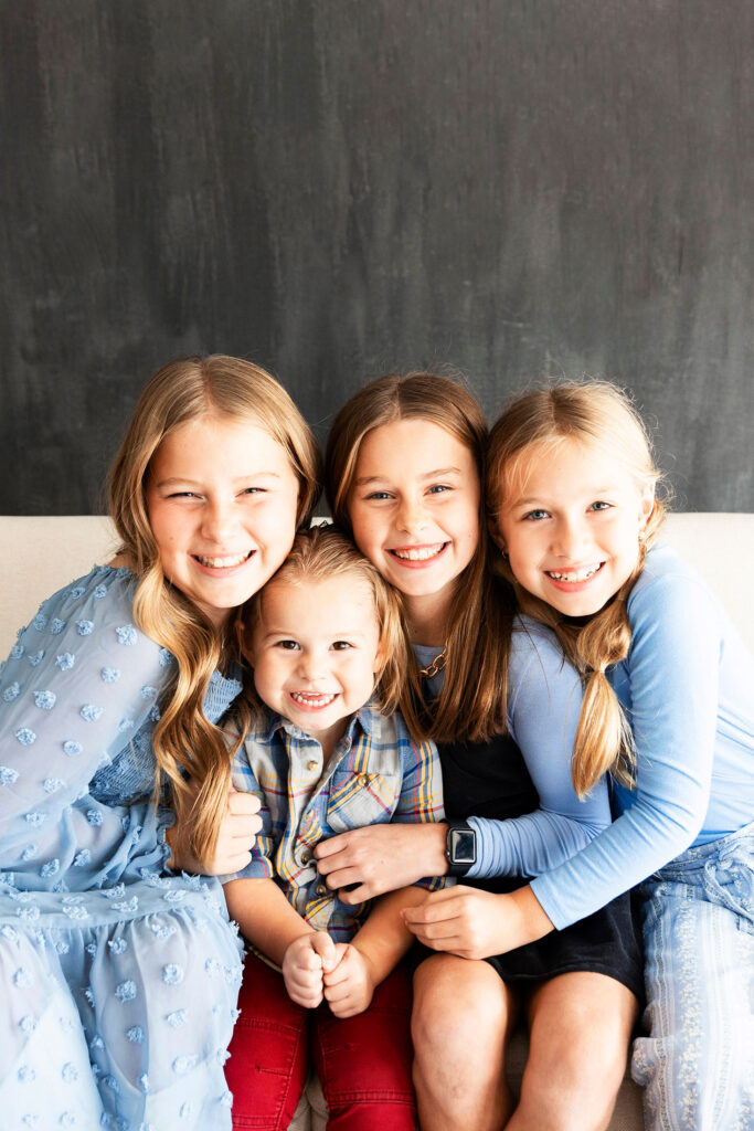 studio of 4 kids hugging on a white sofa