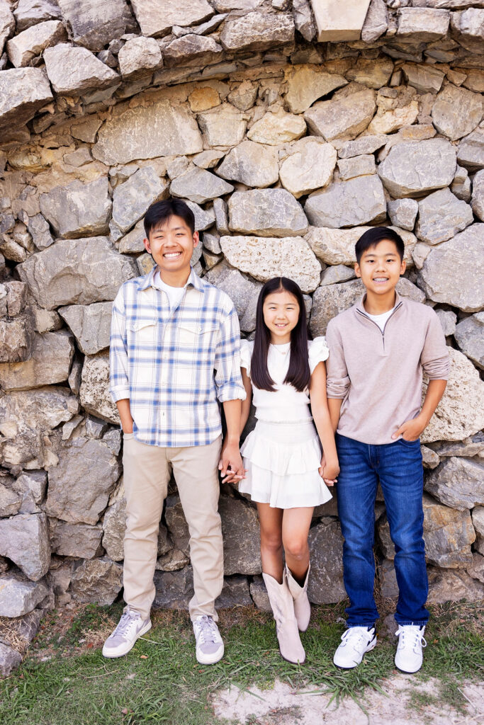 3 kids smiling in front of stone wall
